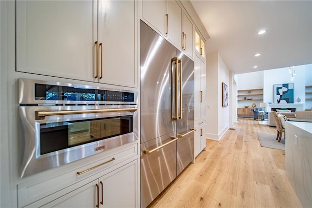 kitchen with light wood-style flooring, recessed lighting, glass insert cabinets, appliances with stainless steel finishes, and open floor plan