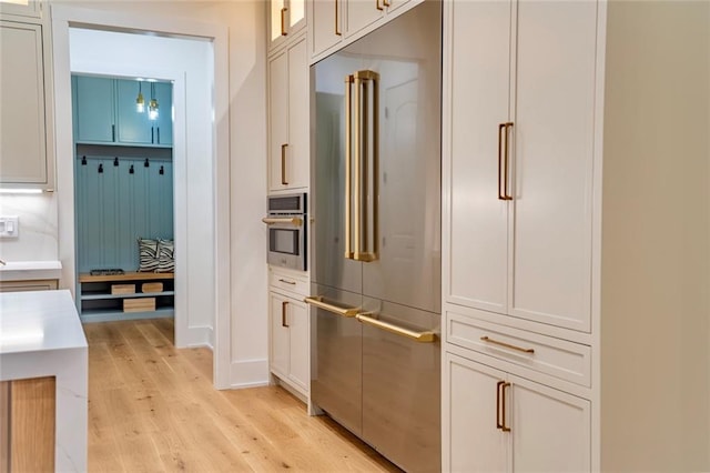 kitchen featuring glass insert cabinets, light countertops, light wood-type flooring, appliances with stainless steel finishes, and white cabinets