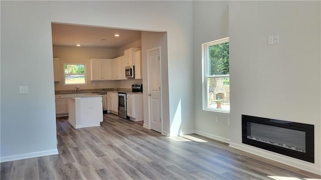 5110 Black Bear Trl, Douglasville, GA 30135 - kitchen featuring stainless steel appliances, white cabinetry, light wood-style flooring, a center island, and a glass covered fireplace