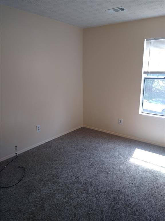 carpeted empty room featuring baseboards, visible vents, and a textured ceiling