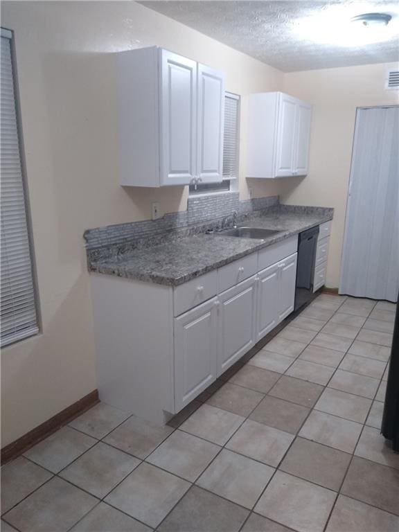 kitchen featuring a sink, black dishwasher, a textured ceiling, white cabinetry, and light tile patterned floors