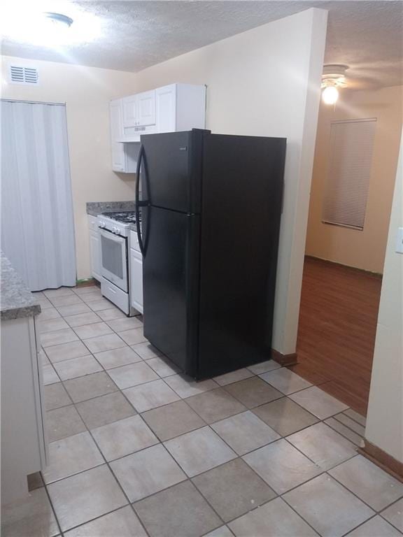 kitchen with visible vents, white gas stove, freestanding refrigerator, light tile patterned flooring, and white cabinets