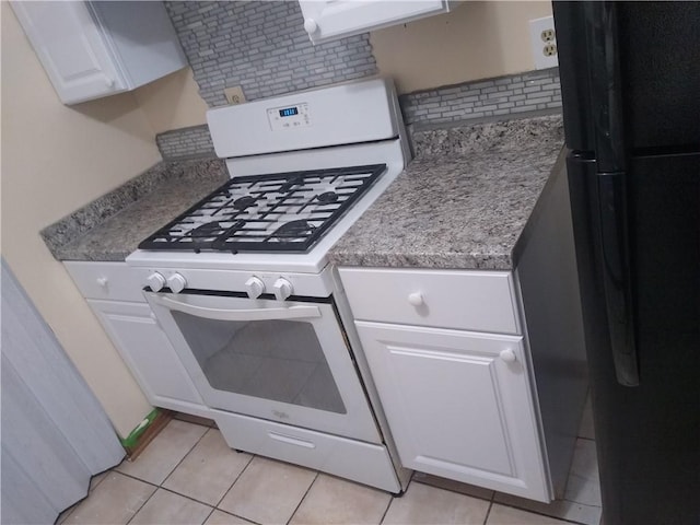 kitchen with tasteful backsplash, gas range gas stove, light tile patterned floors, freestanding refrigerator, and white cabinets