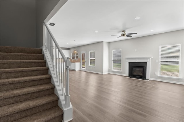 9120 Alden Dr, Locust Grove, GA 30248 - unfurnished living room with stairway, wood finished floors, ceiling fan, a glass covered fireplace, and baseboards