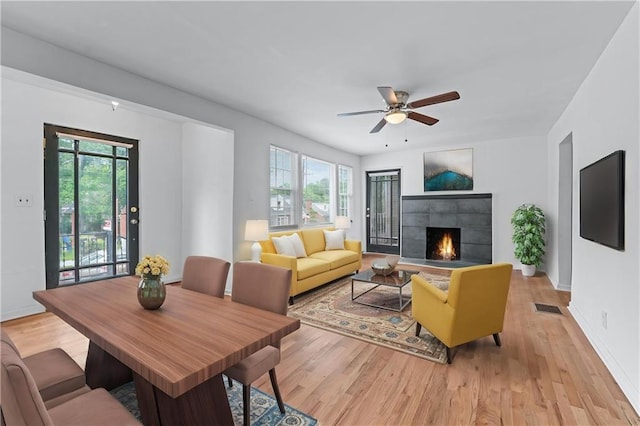 living room featuring a fireplace, light wood-style flooring, a ceiling fan, baseboards, and visible vents