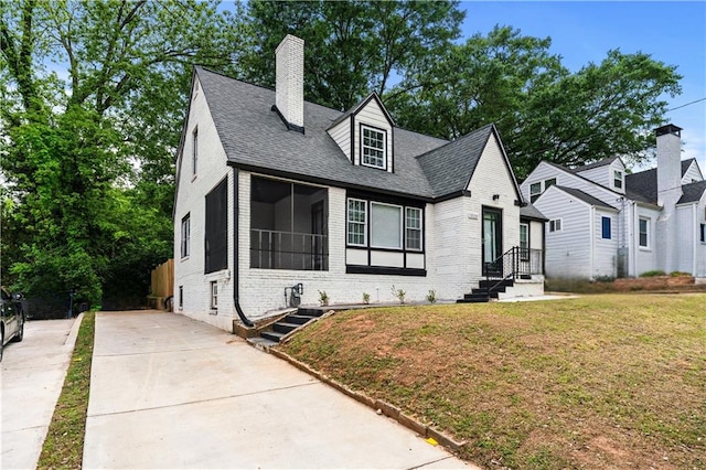 view of front of home featuring a chimney, driveway, a front lawn, and brick siding
