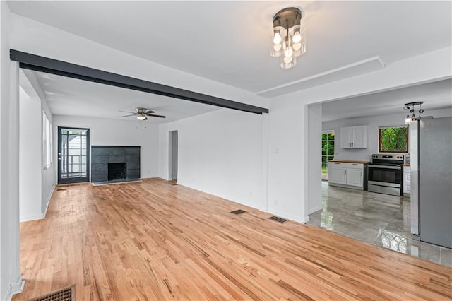 unfurnished living room featuring visible vents, light wood-type flooring, a tile fireplace, baseboards, and ceiling fan with notable chandelier