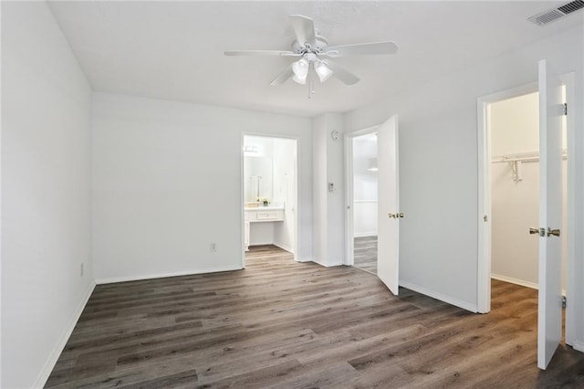 unfurnished bedroom featuring a closet, dark wood-type flooring, ensuite bath, and a spacious closet