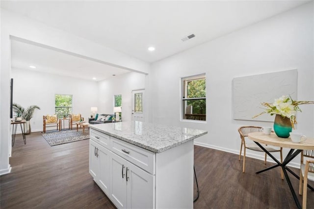 kitchen with light stone counters, dark wood-style floors, visible vents, and a kitchen island