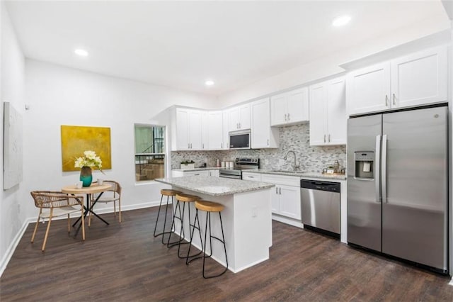 kitchen with a kitchen bar, a sink, backsplash, a center island, and appliances with stainless steel finishes