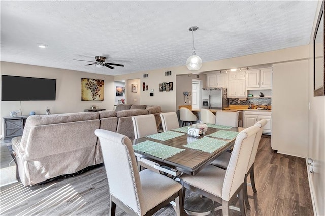 dining space featuring visible vents, a textured ceiling, dark wood-type flooring, and a ceiling fan