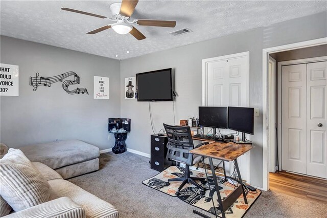 office space featuring visible vents, baseboards, ceiling fan, carpet, and a textured ceiling