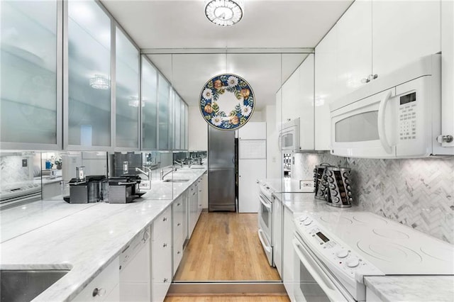 kitchen with white cabinetry, tasteful backsplash, white appliances, light stone countertops, and light hardwood / wood-style floors