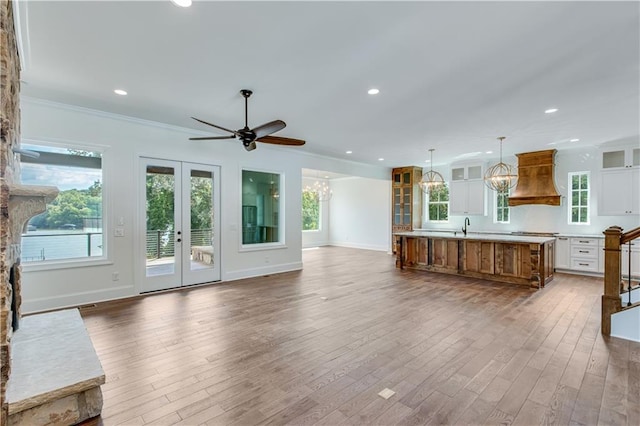 unfurnished living room featuring ornamental molding, french doors, hardwood / wood-style flooring, sink, and ceiling fan with notable chandelier