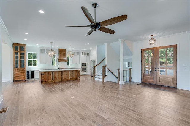 unfurnished living room featuring ceiling fan with notable chandelier, french doors, ornamental molding, and plenty of natural light