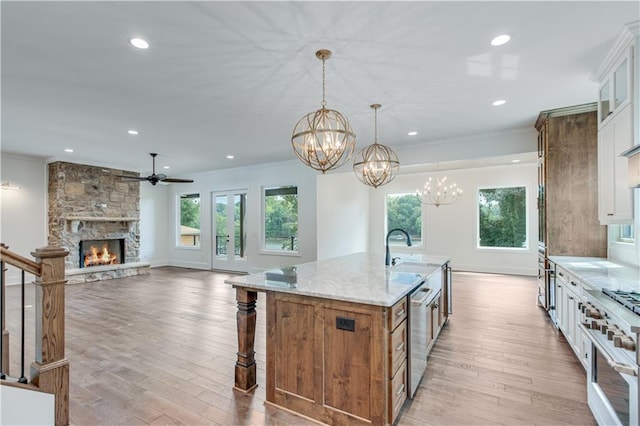 kitchen featuring stainless steel appliances, white cabinetry, light stone countertops, a kitchen island with sink, and a stone fireplace