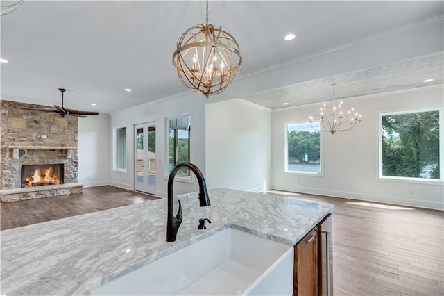 kitchen featuring a stone fireplace, ornamental molding, pendant lighting, light stone counters, and sink