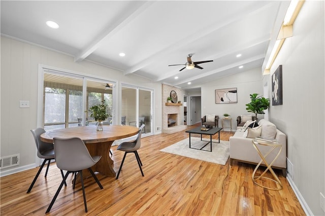 dining space with vaulted ceiling with beams, ceiling fan, a brick fireplace, and light hardwood / wood-style flooring