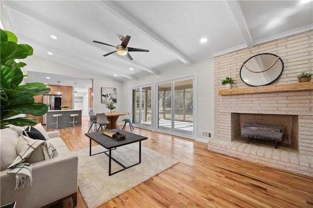 living room with ceiling fan, a brick fireplace, lofted ceiling with beams, and light hardwood / wood-style flooring