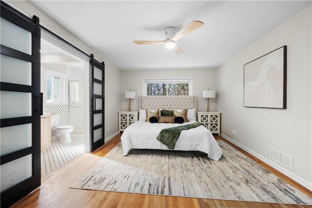 bedroom featuring ensuite bathroom, a barn door, ceiling fan, and light hardwood / wood-style floors