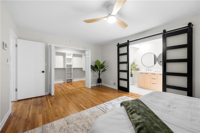 bedroom featuring ensuite bathroom, hardwood / wood-style floors, a spacious closet, ceiling fan, and a barn door