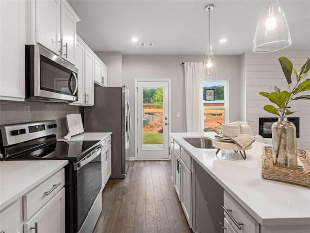 kitchen with dark wood-style floors, stainless steel appliances, light countertops, decorative backsplash, and a sink