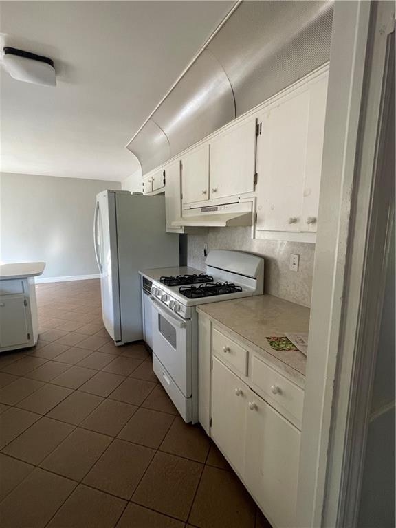 kitchen featuring tasteful backsplash, under cabinet range hood, white cabinets, white appliances, and dark tile patterned flooring