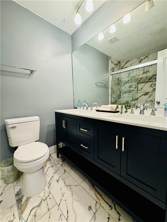 bathroom with vanity, a shower with door, toilet, and a textured ceiling