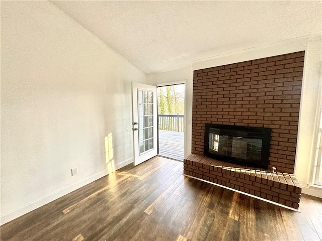 unfurnished living room featuring lofted ceiling, dark hardwood / wood-style floors, a brick fireplace, and a textured ceiling