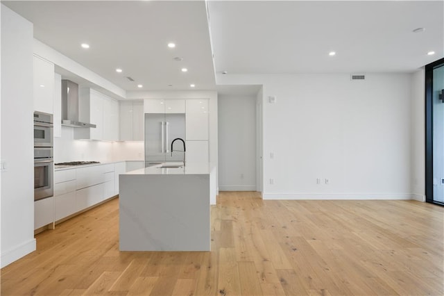 kitchen with a sink, wall chimney range hood, white cabinets, stainless steel appliances, and modern cabinets