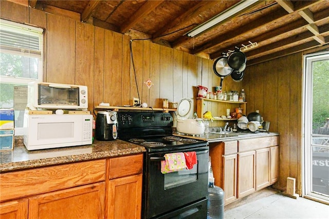 kitchen featuring black range with electric stovetop, white microwave, wood walls, brown cabinets, and concrete floors