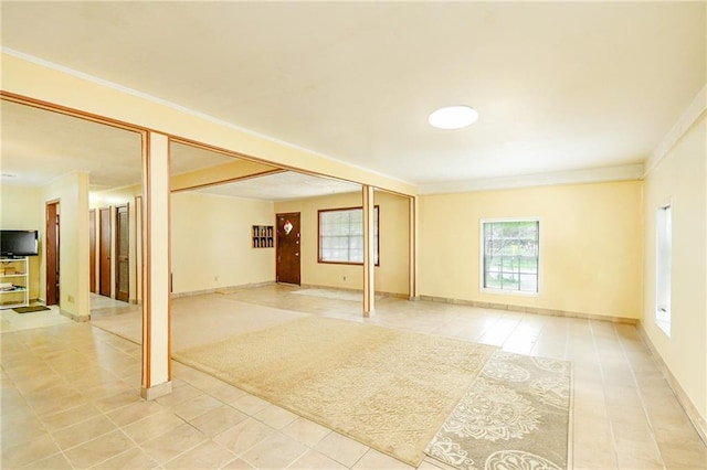 unfurnished living room with light tile patterned floors, ornamental molding, and baseboards