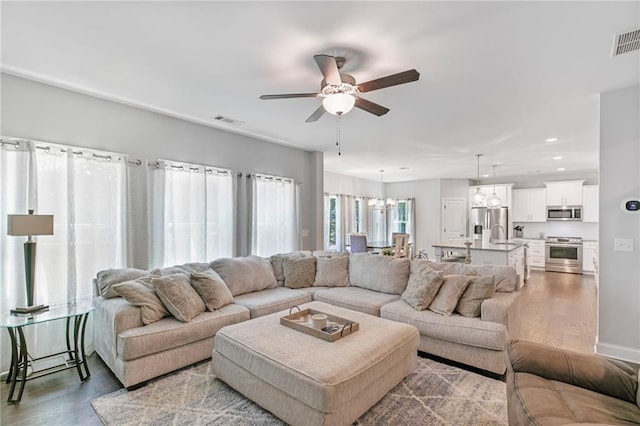 living room with ceiling fan with notable chandelier, wood finished floors, visible vents, and recessed lighting