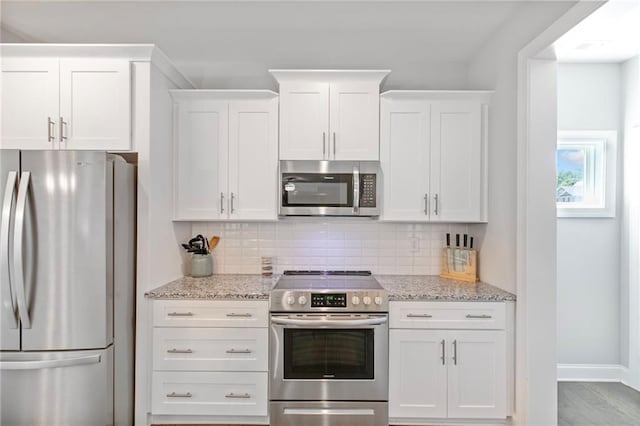 kitchen featuring appliances with stainless steel finishes, white cabinets, decorative backsplash, and light stone countertops