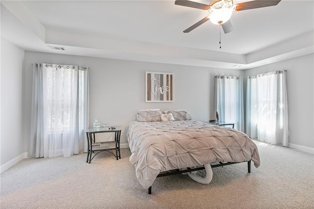 bedroom featuring baseboards, visible vents, a raised ceiling, a ceiling fan, and light colored carpet