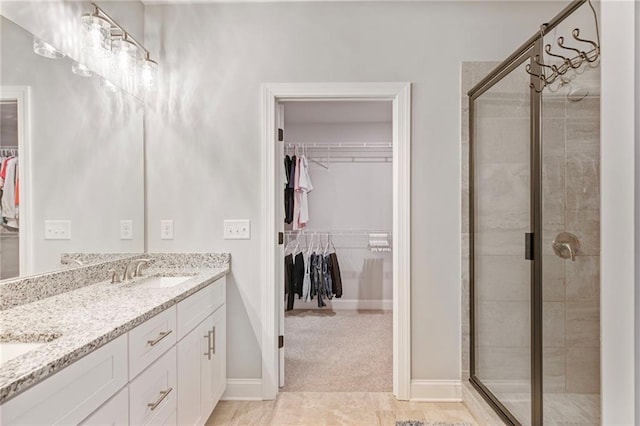 full bathroom with a walk in closet, double vanity, a sink, a shower stall, and baseboards