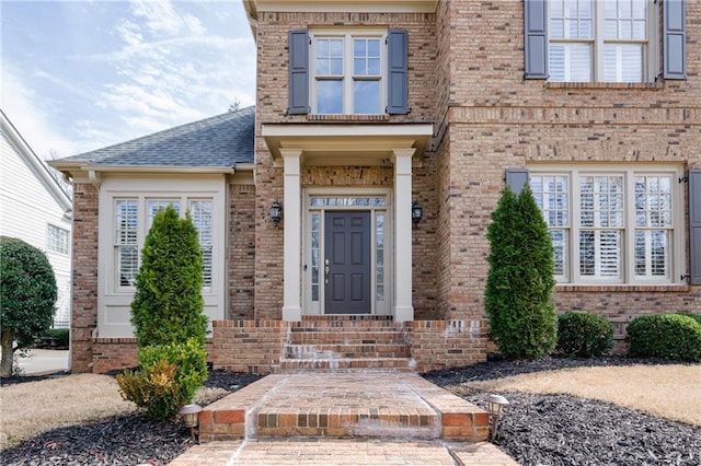 entrance to property with a shingled roof and brick siding