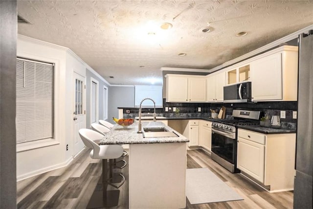 kitchen featuring gas stove, a kitchen bar, decorative backsplash, an island with sink, and ornamental molding