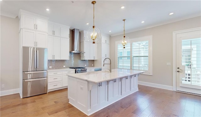 kitchen with wall chimney range hood, sink, appliances with stainless steel finishes, white cabinetry, and a center island with sink