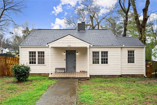 bungalow-style home with a front lawn, fence, roof with shingles, and a chimney