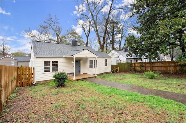 back of house featuring a yard, roof with shingles, a fenced backyard, and a chimney