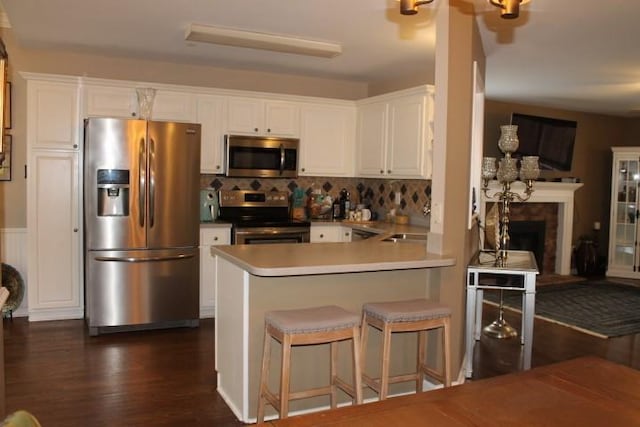 kitchen with tasteful backsplash, dark wood finished floors, a fireplace, stainless steel appliances, and white cabinetry