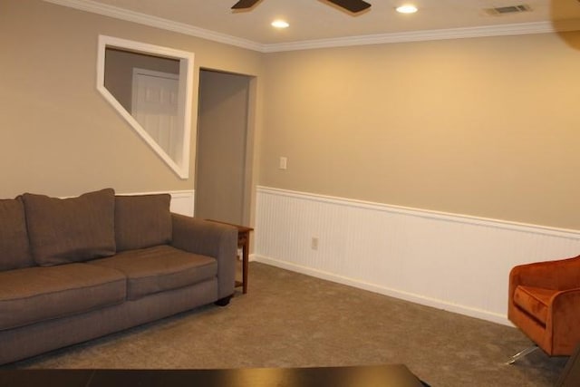 living area with visible vents, ornamental molding, a ceiling fan, carpet floors, and wainscoting