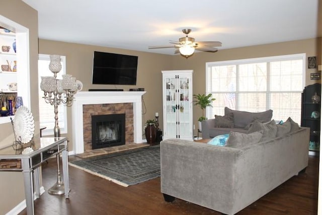 living room with a fireplace with raised hearth, dark wood-type flooring, and ceiling fan