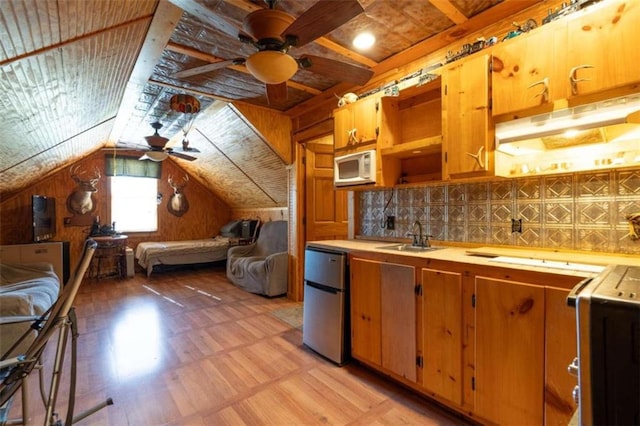 kitchen featuring sink, ceiling fan, lofted ceiling, wooden walls, and stainless steel refrigerator