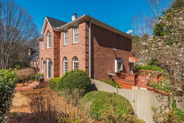 view of property exterior featuring brick siding, fence, a chimney, and a wooden deck