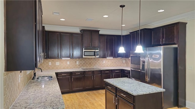 kitchen with sink, crown molding, appliances with stainless steel finishes, pendant lighting, and light stone countertops