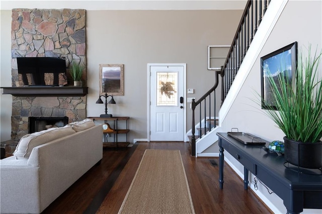 entrance foyer with stairway, baseboards, a stone fireplace, and wood finished floors