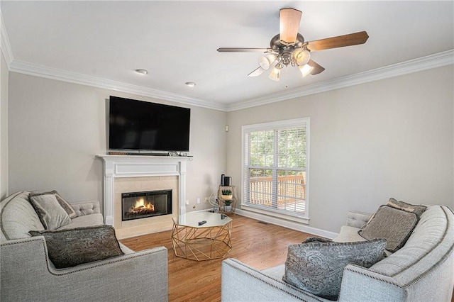 living area featuring ornamental molding, wood finished floors, a ceiling fan, a tile fireplace, and baseboards