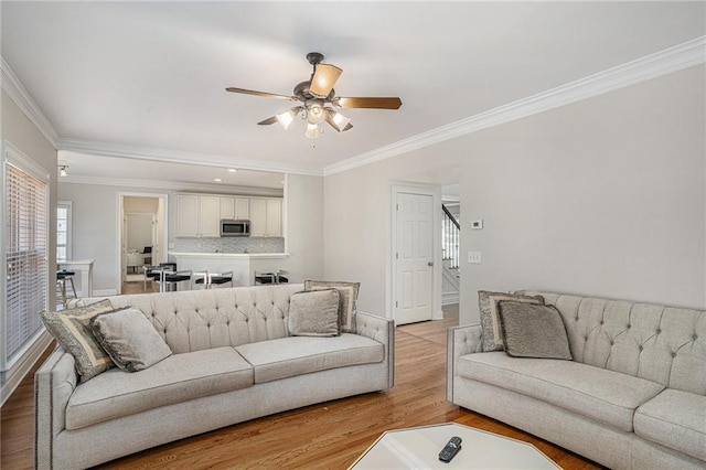 living room with stairs, crown molding, light wood-style flooring, ceiling fan, and baseboards